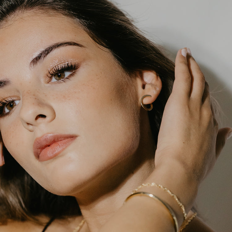 Sleek open hoop earrings in gold vermeil worn on ear showing twisted design