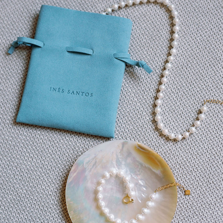 Pearl necklace and bracelet on a shell with an Inês Santos jewellery pouch.