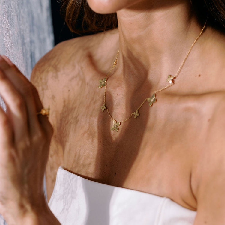 Close-up of a person wearing a delicate gold necklace with floral pendants.