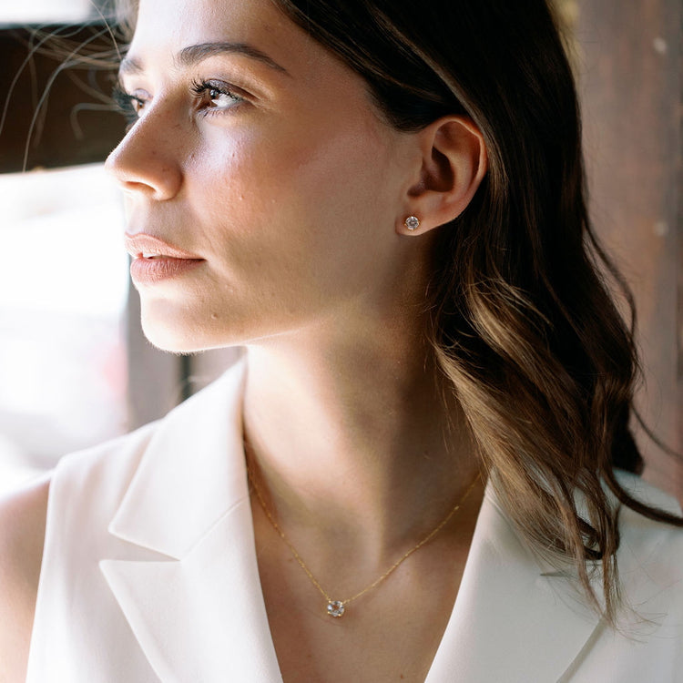 Woman wearing a gold vermeil necklace and white topaz stud earrings with a blurred background
