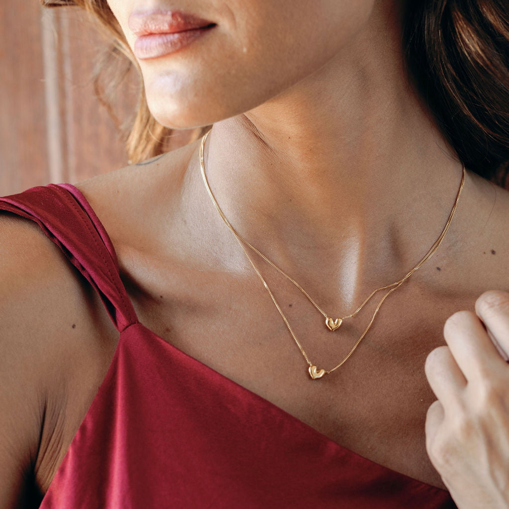 Close-up of a woman wearing two gold vermeil necklaces of different sizes with heart pendants.