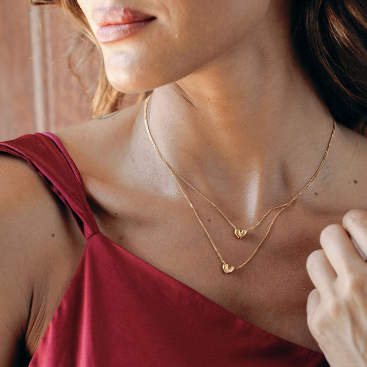 Close-up of a woman wearing two gold vermeil necklaces of different sizes with heart pendants.